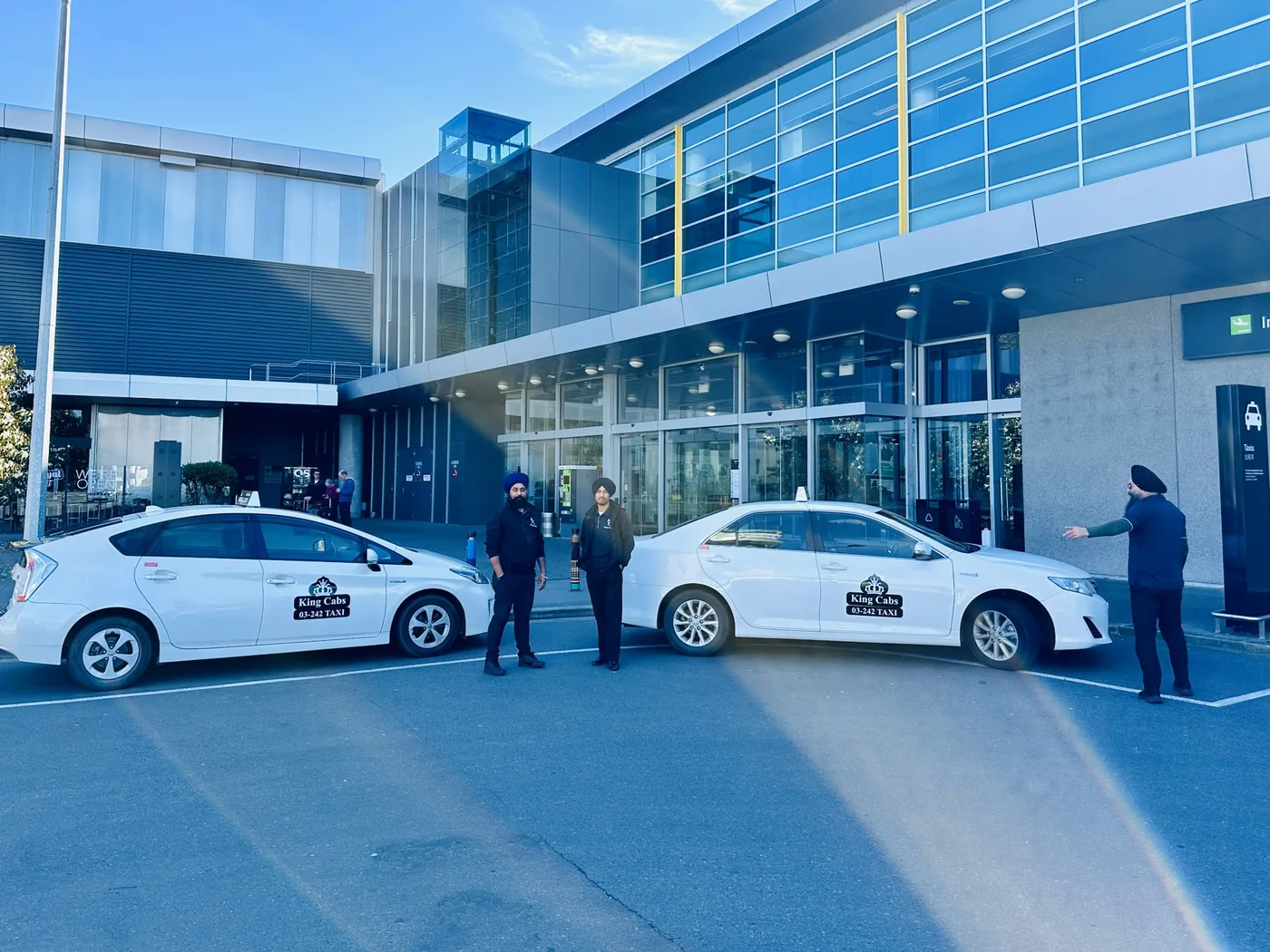 Taxi Christchurch – King Cabs 2 Two white King Cabs taxis and drivers outside Christchurch Airport terminal
